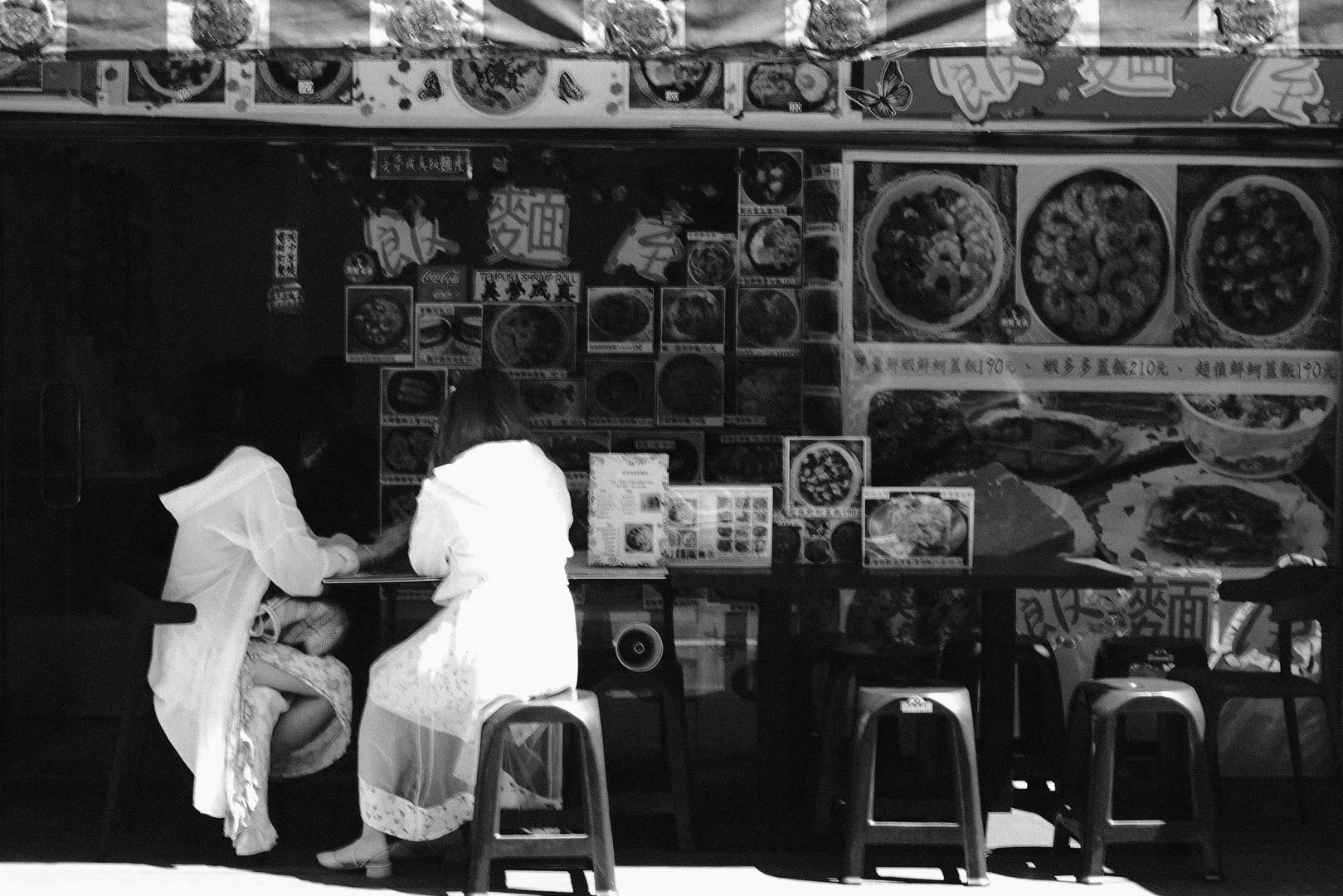 街邊小吃店前兩名顧客坐在吧台旁，強烈陽光照亮白色衣服，牆面貼滿餐點圖像，365 Project September 26