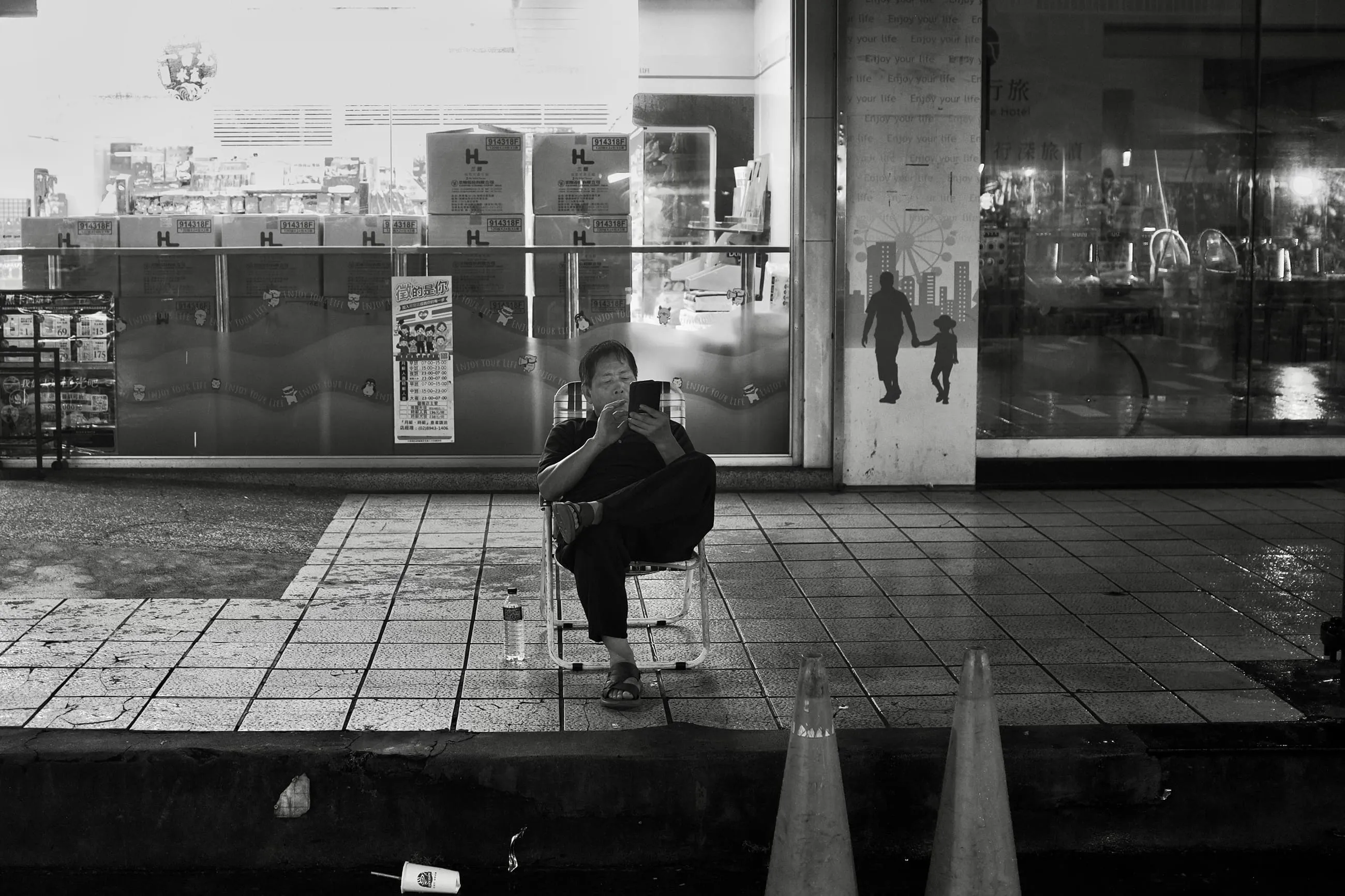 夜間騎樓前一人坐在摺疊椅上低頭看手機，身旁放著水瓶，365 Project October 11