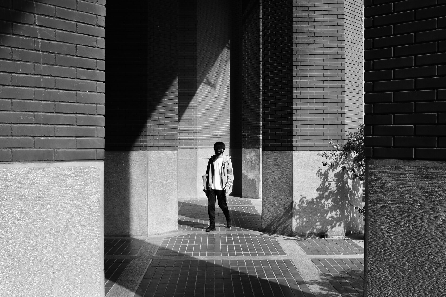 Black and white urban geometry scene with brick columns, sharp shadows, and a lone figure walking through an arcade in Taiwan