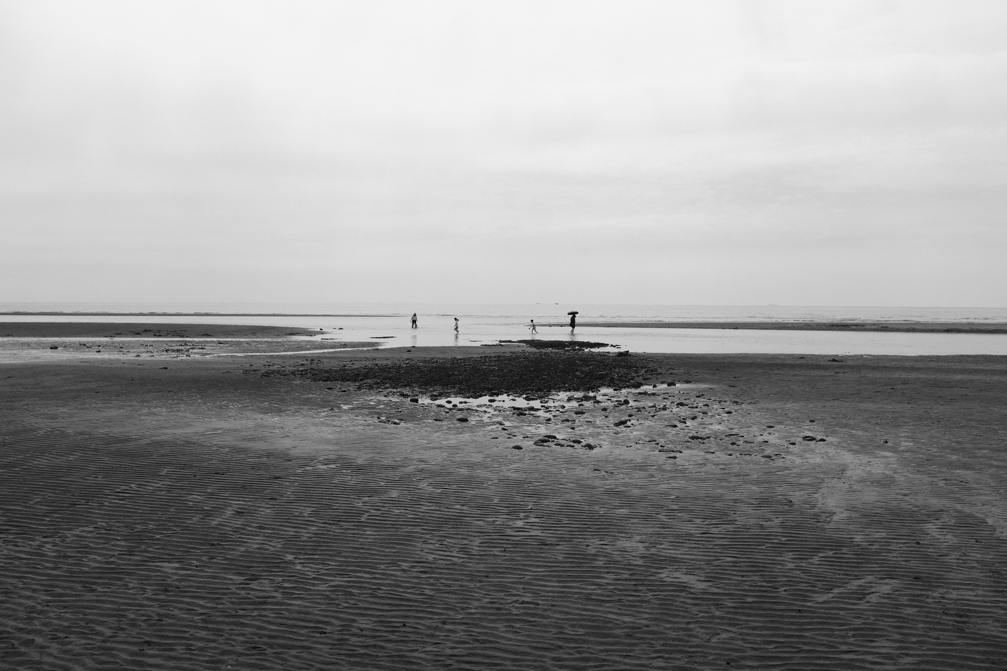 Black and white tidal flat landscape with small distant figures walking across shallow water in Taiwan