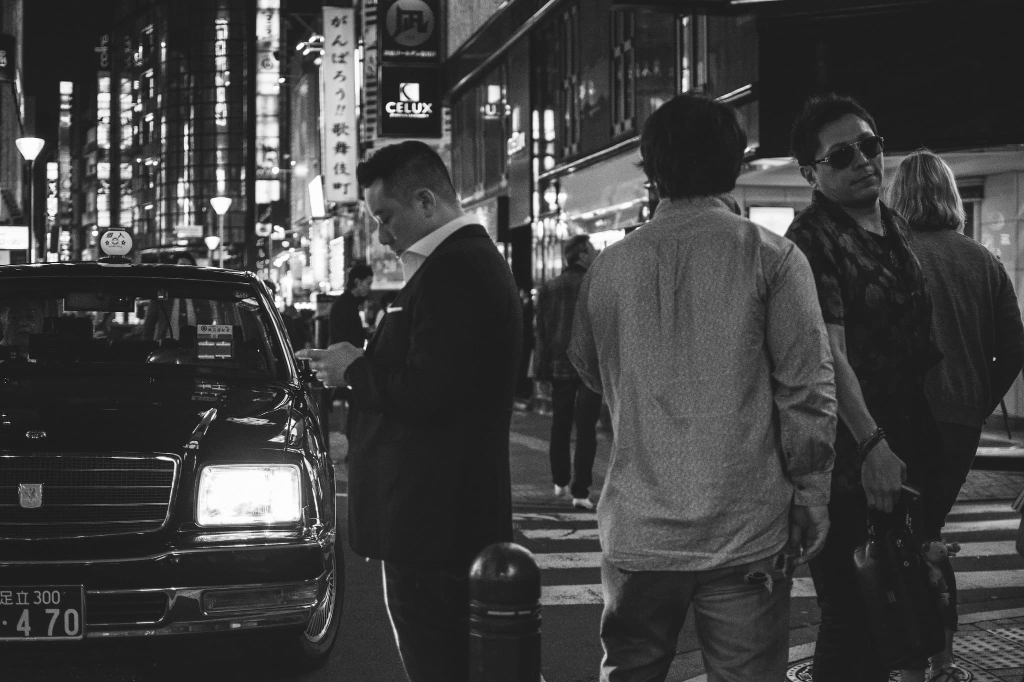 Black and white night street in Japan with a parked taxi and pedestrians gathered beneath illuminated signs - JAPAN project cover