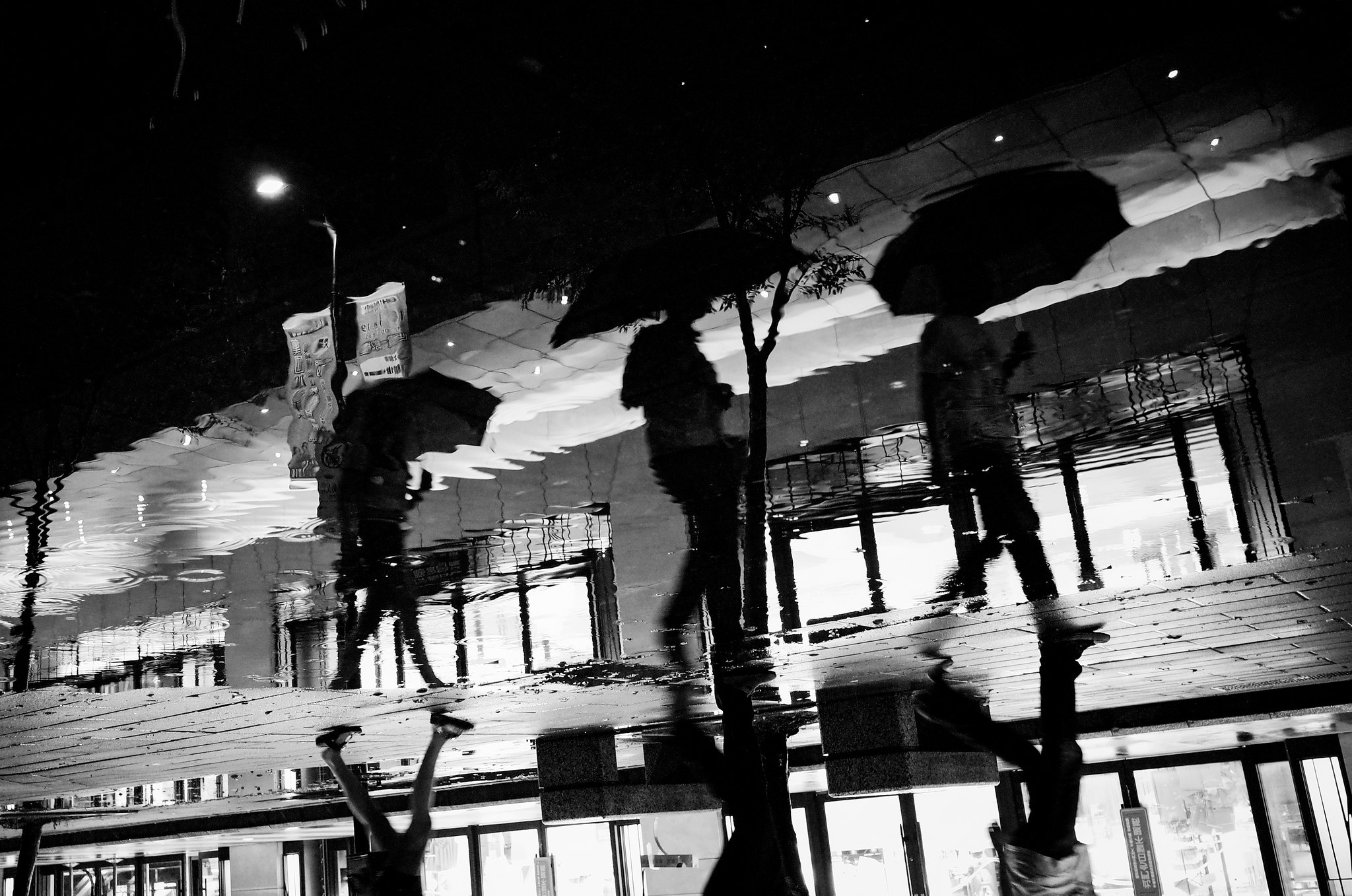 Black and white rainy night street scene with umbrellas reflected in wet pavement in Taiwan