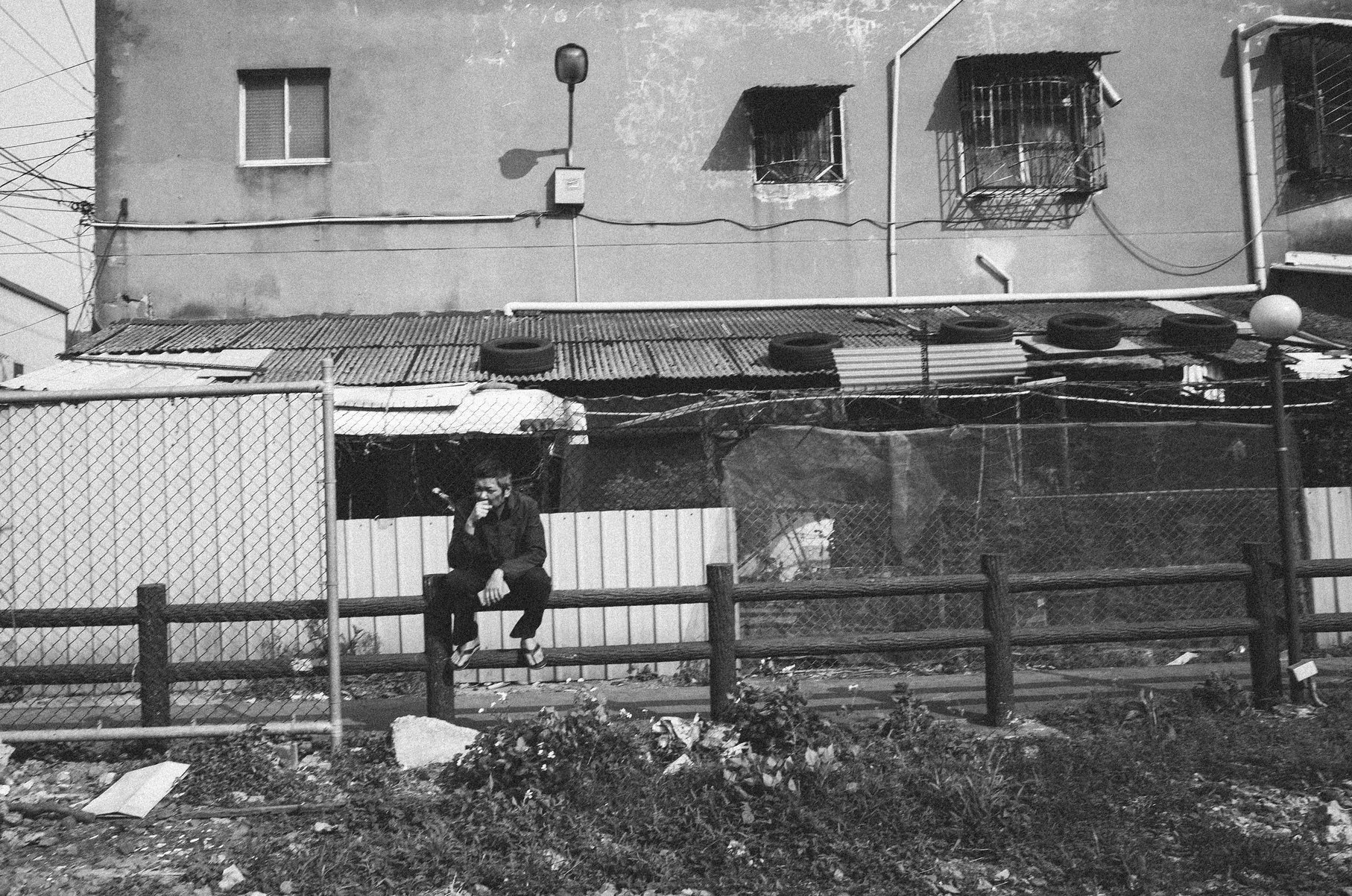 Black and white street photograph of a person with an umbrella walking beside layered fencing in the rain in Taiwan