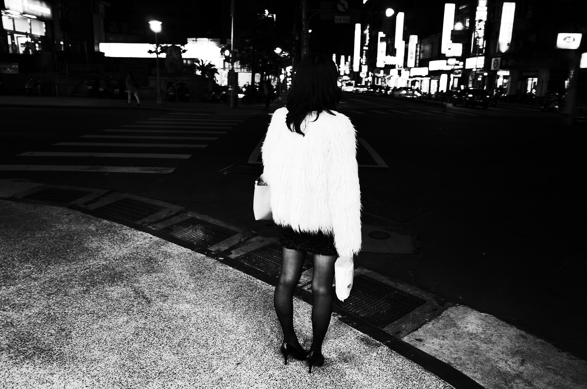 Black and white street photograph of a woman from behind, wearing a furry coat at a city intersection at night - SOMEWHERE project cover